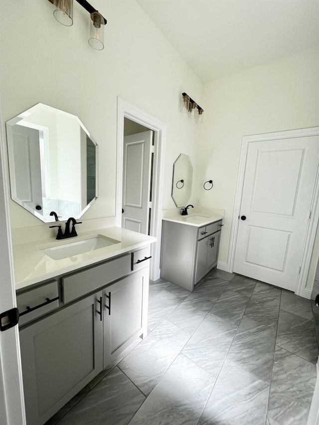 bathroom featuring marble finish flooring, two vanities, and baseboards