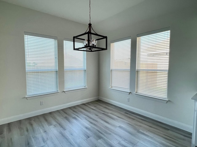 unfurnished dining area with a chandelier, wood finished floors, baseboards, and plenty of natural light