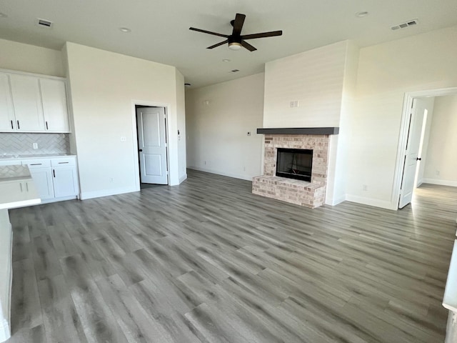 unfurnished living room featuring a ceiling fan, wood finished floors, baseboards, and a fireplace