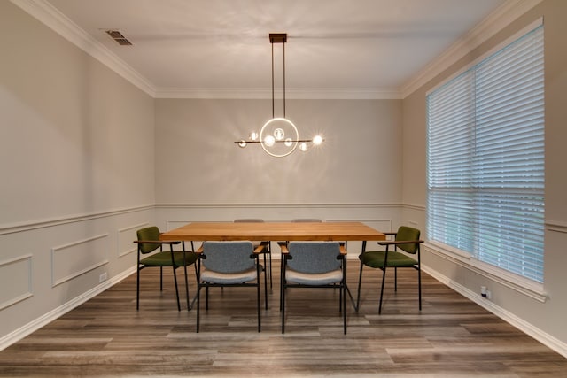 dining room with wood finished floors, ornamental molding, a chandelier, a wainscoted wall, and a decorative wall
