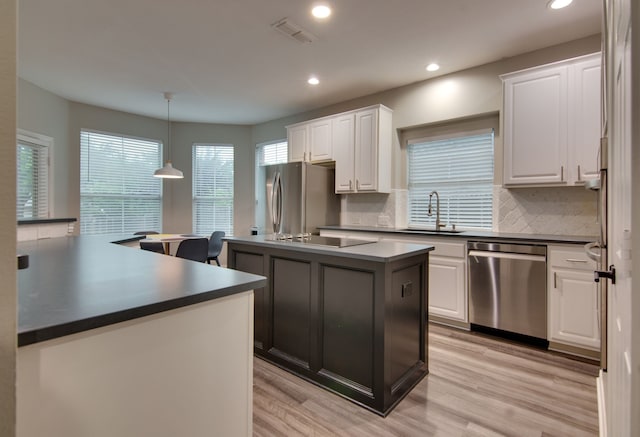 kitchen with stainless steel appliances, a sink, dark countertops, a kitchen island, and recessed lighting