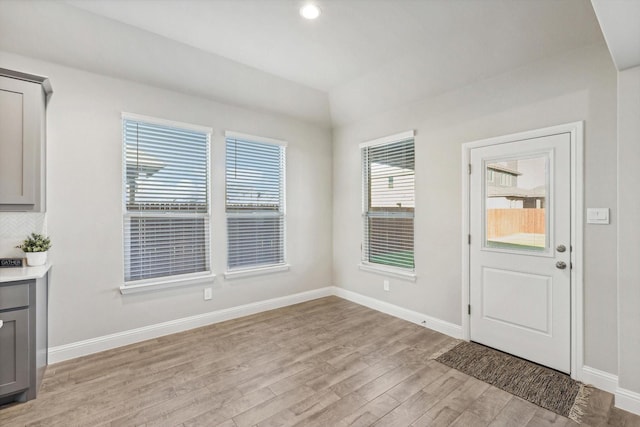 unfurnished dining area featuring light wood-style flooring, baseboards, and lofted ceiling