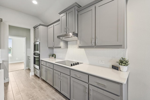 kitchen with gray cabinetry, stainless steel appliances, under cabinet range hood, tasteful backsplash, and light countertops