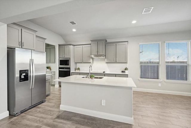 kitchen with appliances with stainless steel finishes, gray cabinets, a sink, light countertops, and an island with sink