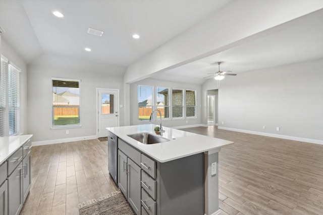 kitchen with gray cabinetry, a sink, stainless steel dishwasher, vaulted ceiling, and light wood-style flooring