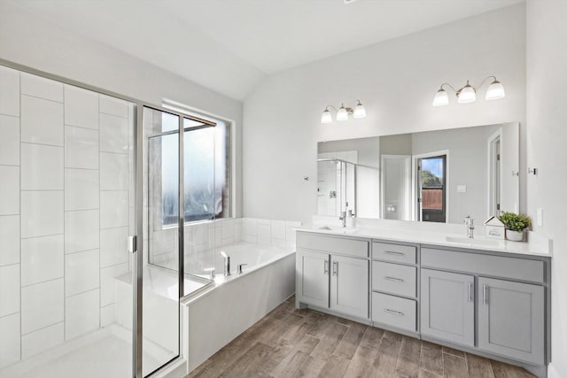 full bathroom with a stall shower, a garden tub, double vanity, wood finished floors, and vaulted ceiling