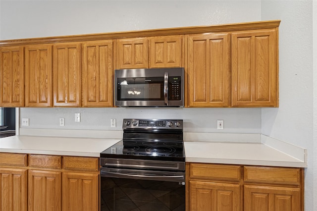 kitchen featuring stainless steel microwave, black range with electric cooktop, brown cabinetry, and light countertops