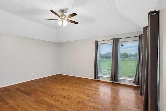 unfurnished room with a ceiling fan, vaulted ceiling, wood finished floors, a textured ceiling, and baseboards