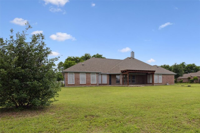 back of house with a lawn, a chimney, and brick siding