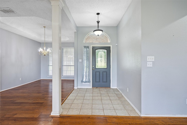 foyer with light wood-type flooring, a textured ceiling, decorative columns, and baseboards