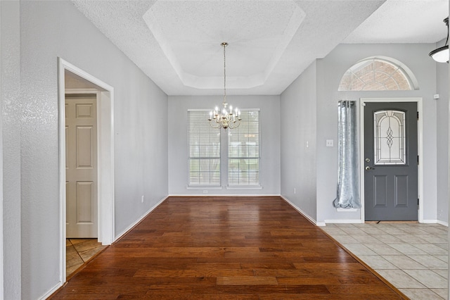 entryway featuring wood finished floors, a textured ceiling, healthy amount of natural light, a chandelier, and a tray ceiling