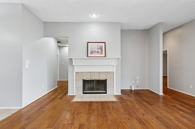 unfurnished living room with a tiled fireplace, hardwood / wood-style floors, and baseboards