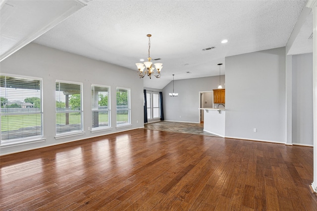 unfurnished living room with a chandelier, wood finished floors, a textured ceiling, vaulted ceiling, and baseboards
