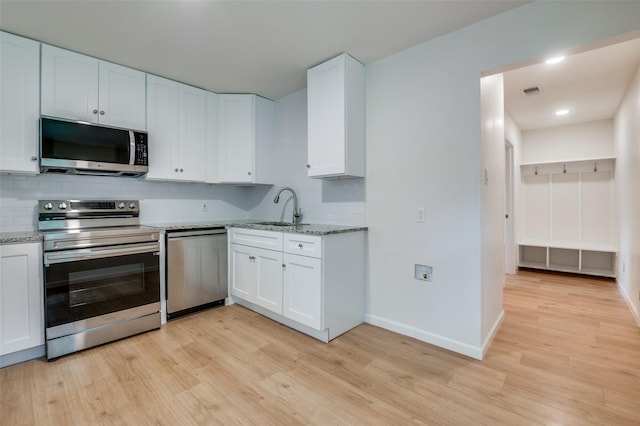 kitchen with appliances with stainless steel finishes, a sink, decorative backsplash, light wood finished floors, and white cabinets