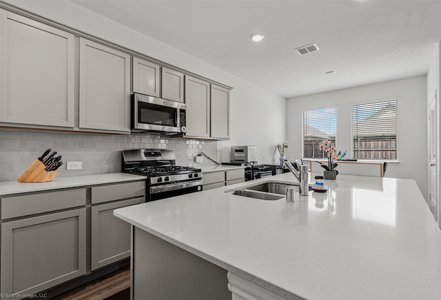 kitchen featuring stainless steel appliances, gray cabinetry, a sink, backsplash, and recessed lighting