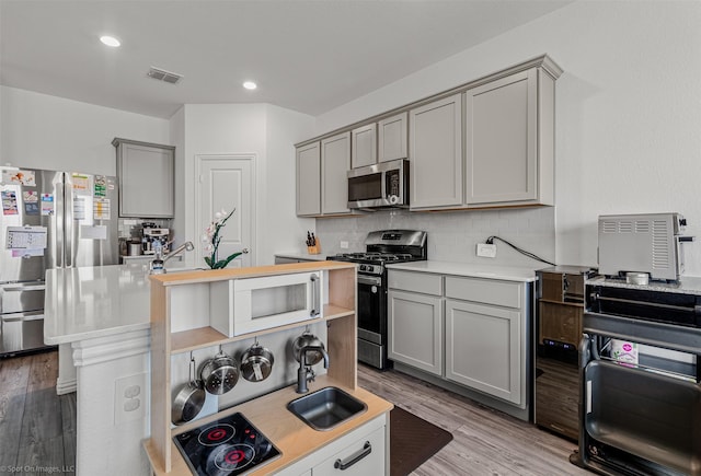 kitchen featuring stainless steel appliances, gray cabinets, a sink, light countertops, and tasteful backsplash