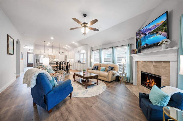 living room with arched walkways, a ceiling fan, a fireplace, wood finished floors, and lofted ceiling