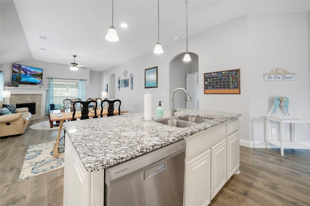 kitchen with stainless steel dishwasher, a sink, light wood finished floors, a fireplace, and vaulted ceiling