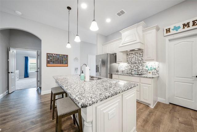 kitchen featuring a sink, stainless steel fridge, custom range hood, arched walkways, and light stone counters