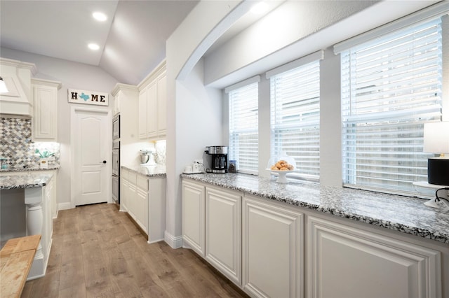 kitchen with backsplash, white cabinetry, light wood finished floors, stainless steel microwave, and lofted ceiling