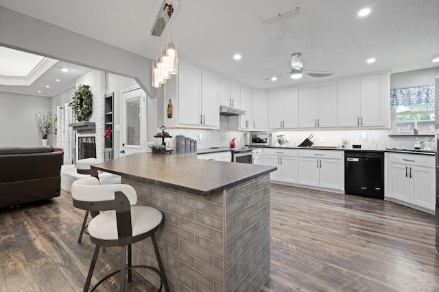 kitchen with black dishwasher, dark countertops, under cabinet range hood, a peninsula, and white cabinets