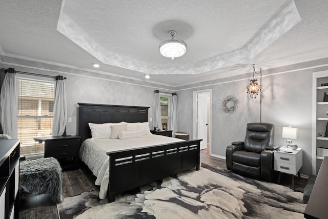 bedroom with a textured ceiling, a raised ceiling, wood finished floors, crown molding, and multiple windows