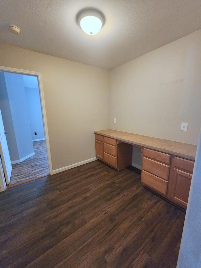 unfurnished office with built in study area, dark wood-style floors, baseboards, and a textured ceiling