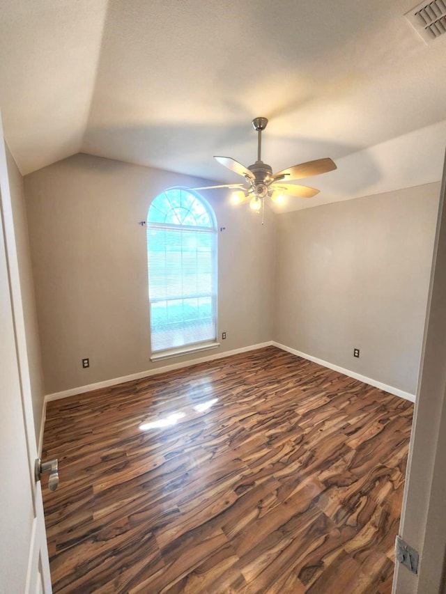 empty room featuring dark wood-type flooring, a ceiling fan, vaulted ceiling, and baseboards