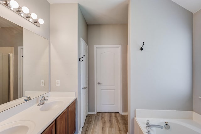 bathroom with a bath, wood finished floors, double vanity, and baseboards