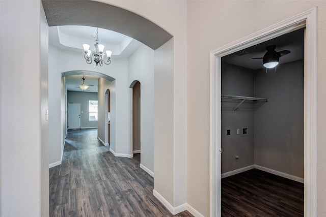 hallway with arched walkways, dark wood-type flooring, a chandelier, baseboards, and a tray ceiling