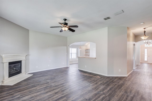 unfurnished living room featuring arched walkways, dark wood finished floors, baseboards, and a ceiling fan