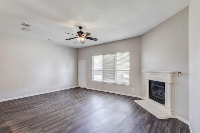 unfurnished living room with a glass covered fireplace, dark wood-type flooring, baseboards, and a ceiling fan