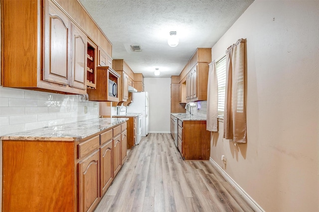 kitchen with light wood-style flooring, tasteful backsplash, baseboards, brown cabinetry, and a textured ceiling