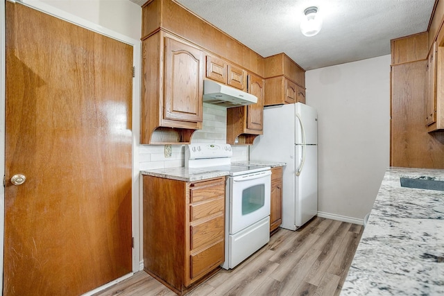 kitchen featuring white appliances, under cabinet range hood, light wood-type flooring, backsplash, and light stone countertops