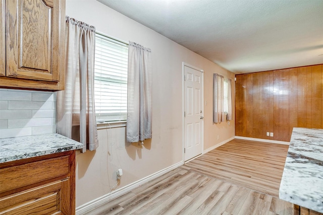 entryway featuring light wood-type flooring, baseboards, wood walls, and a textured ceiling