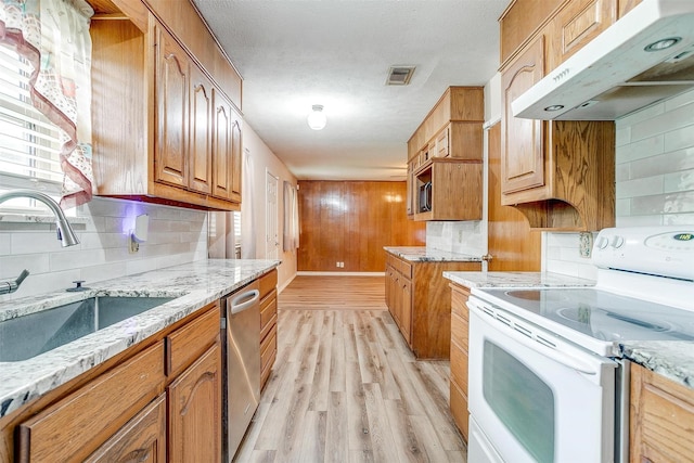 kitchen with electric range, under cabinet range hood, a sink, light stone counters, and backsplash