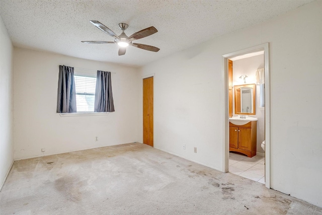 unfurnished bedroom with carpet flooring, connected bathroom, a textured ceiling, ceiling fan, and a sink