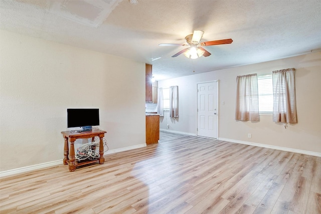 unfurnished living room featuring light wood-style flooring, a ceiling fan, healthy amount of natural light, baseboards, and a textured ceiling
