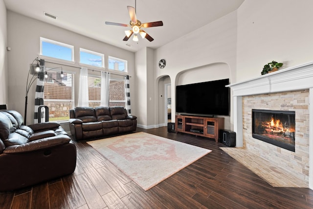 2444 Kingsgate Dr, Little Elm, TX 75068 - living room with ceiling fan, a stone fireplace, arched walkways, dark wood-style floors, and a high ceiling