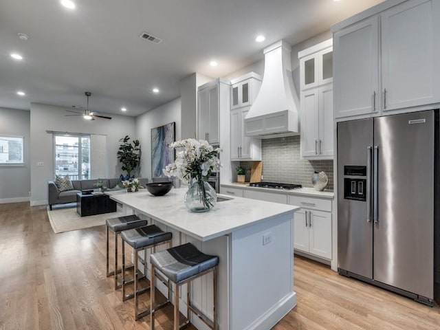 kitchen featuring stainless steel appliances, custom exhaust hood, light wood finished floors, decorative backsplash, and recessed lighting