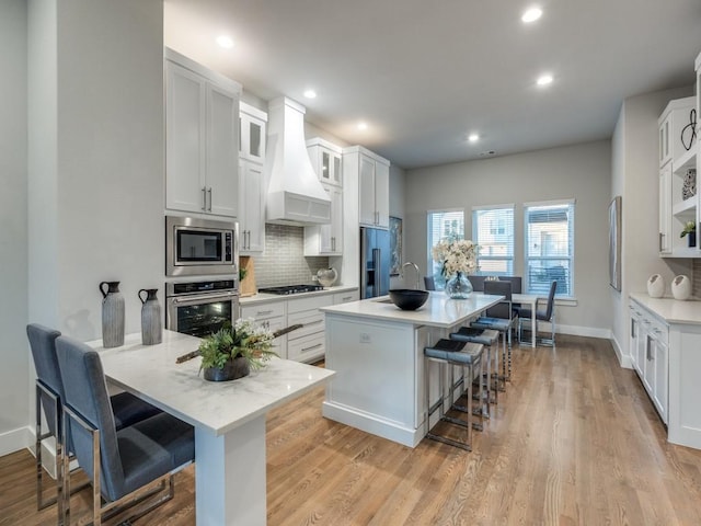 1129 Manderly Ct, Dallas, TX 75204 - kitchen with appliances with stainless steel finishes, a breakfast bar area, custom exhaust hood, decorative backsplash, and white cabinetry