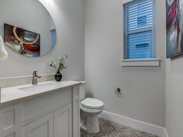 bathroom featuring baseboards, toilet, vanity, and brick patterned floors