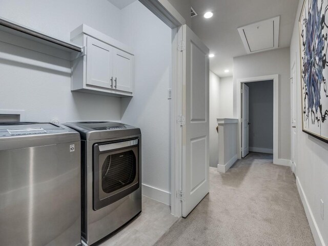 clothes washing area featuring washing machine and dryer, attic access, cabinet space, light colored carpet, and baseboards