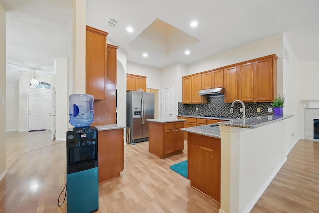 4416 Heath Ct, Plano, TX 75024 - kitchen featuring stainless steel fridge, under cabinet range hood, light wood-style flooring, brown cabinets, and decorative backsplash