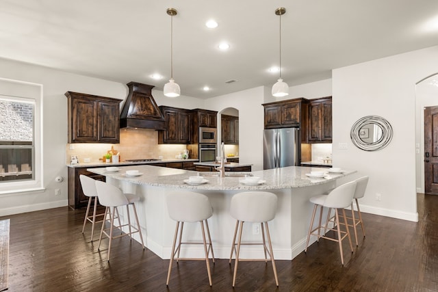 7020 Benjamin Way, Colleyville, TX 76034 - kitchen with stainless steel appliances, custom exhaust hood, arched walkways, a large island with sink, and decorative backsplash