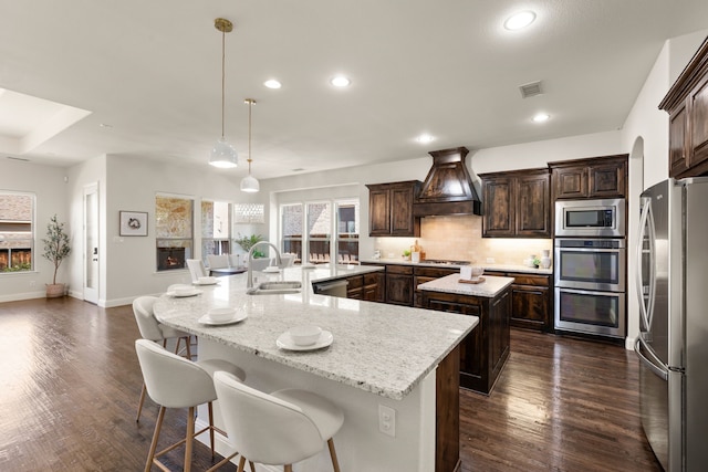 7020 Benjamin Way, Colleyville, TX 76034 - kitchen with stainless steel appliances, a large island with sink, premium range hood, dark brown cabinets, and decorative backsplash