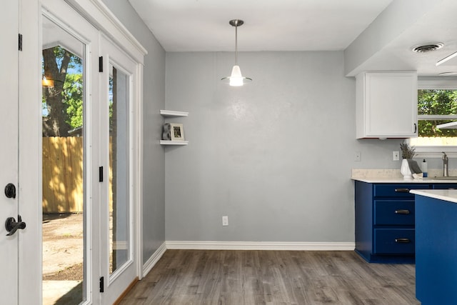 kitchen featuring blue cabinets, wood finished floors, a sink, light countertops, and white cabinets