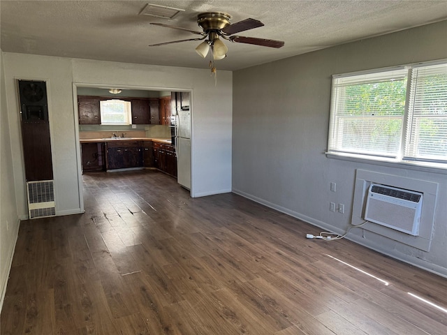 425 S 1st St W, Clyde, TX 79510 - unfurnished living room featuring a wall mounted AC, dark wood-style flooring, a ceiling fan, baseboards, and a textured ceiling