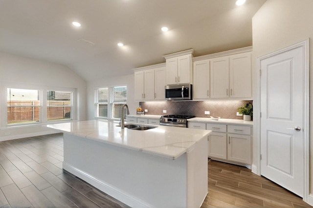 kitchen featuring appliances with stainless steel finishes, a sink, vaulted ceiling, wood finished floors, and backsplash