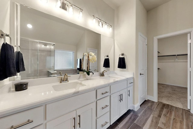 full bath featuring a shower stall, double vanity, a walk in closet, wood finish floors, and baseboards